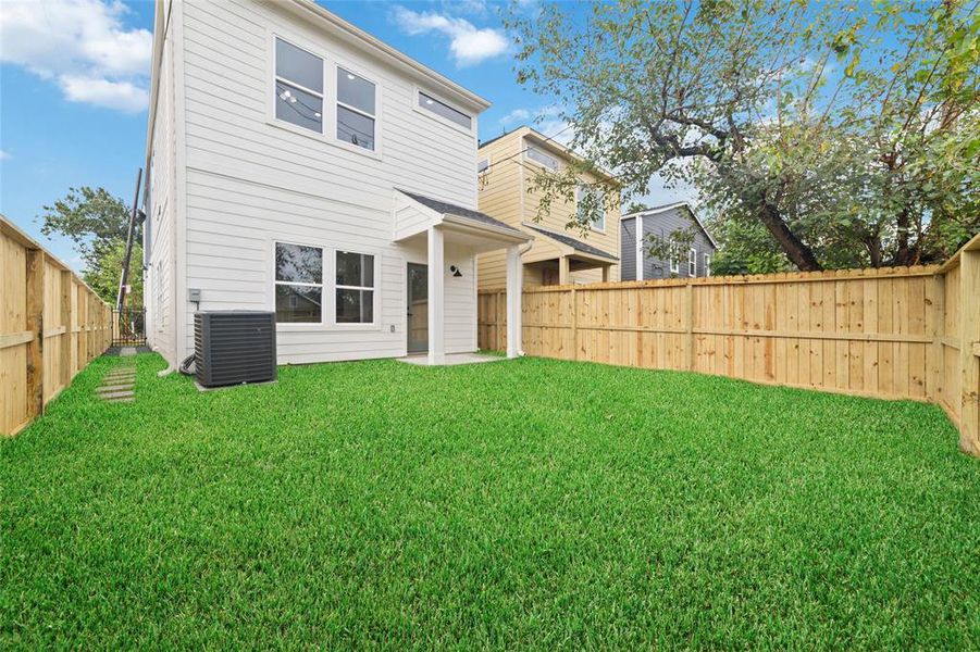 This well-maintained, fenced backyard features lush green grass and a modern air conditioning unit, offering privacy and comfort for outdoor activities.