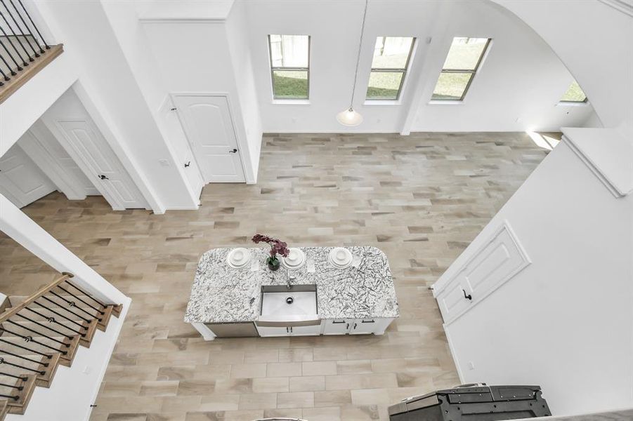 This is a spacious, high-ceilinged interior with large windows, modern design, a neutral color palette, and elegant herringbone patterned flooring. A stylish kitchen island takes center stage in an open-plan layout, adjacent to a staircase with classic wood accents.