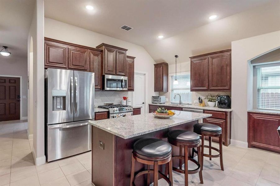 Kitchen with stainless steel appliances, a center island, vaulted ceiling, decorative backsplash, and decorative light fixtures