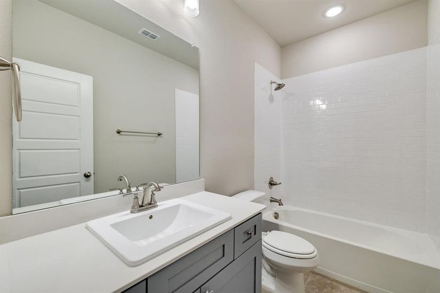 Full bathroom with vanity, tiled shower / bath combo, toilet, and tile patterned floors