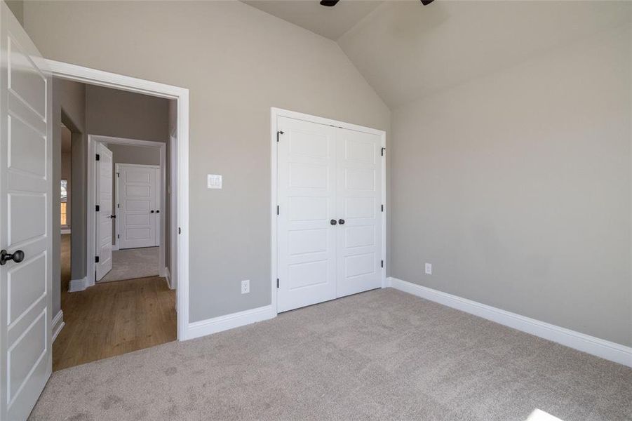 Unfurnished bedroom featuring carpet flooring, lofted ceiling, a closet, and ceiling fan