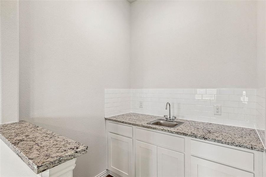 Kitchen featuring sink, light stone counters, backsplash, and white cabinetry