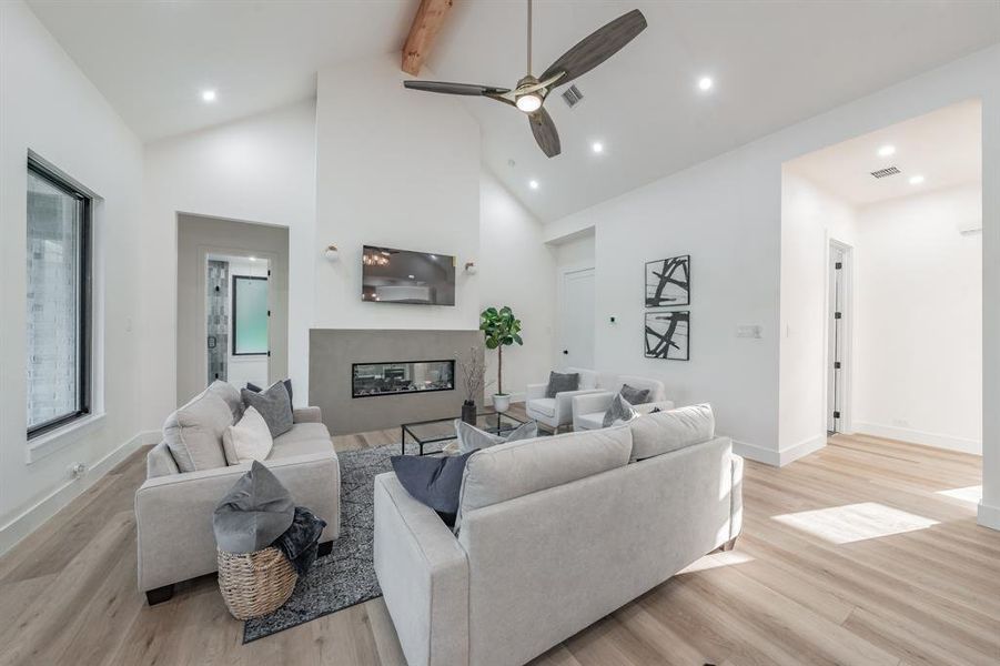 Living room featuring a fireplace, blonde plank, wood-like luxury vinyl floors, beam ceiling, high vaulted ceiling, and ceiling fan