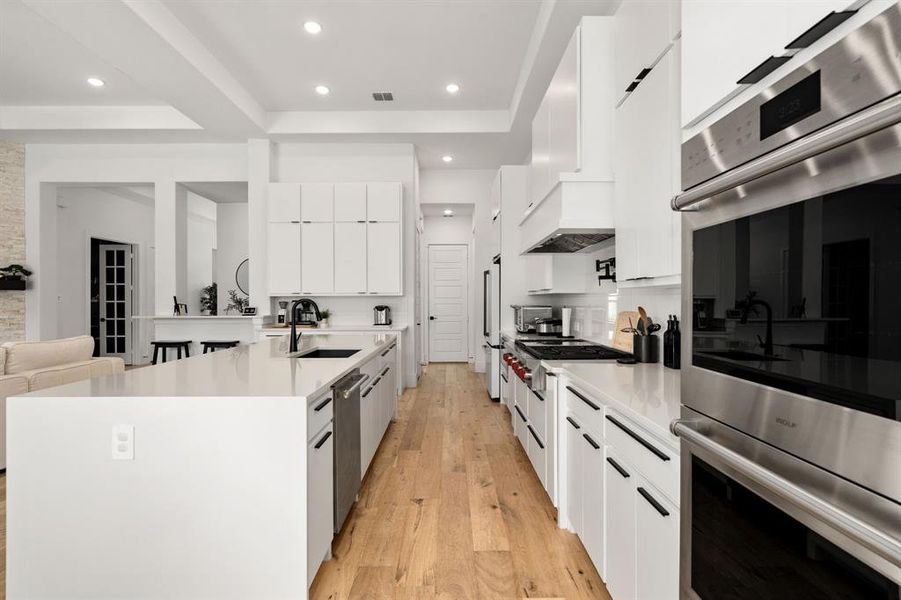 Kitchen with stainless steel appliances, light wood-type flooring, custom range hood, sink, and white cabinetry