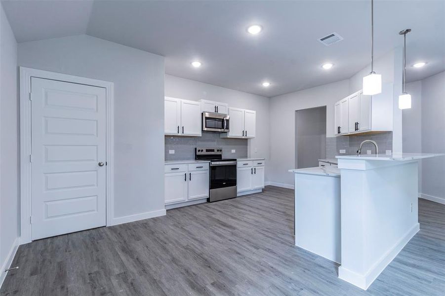 Kitchen featuring white cabinets, appliances with stainless steel finishes, hanging light fixtures, and kitchen peninsula