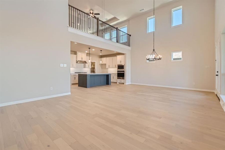 Unfurnished living room with light hardwood / wood-style floors, a notable chandelier, and a high ceiling