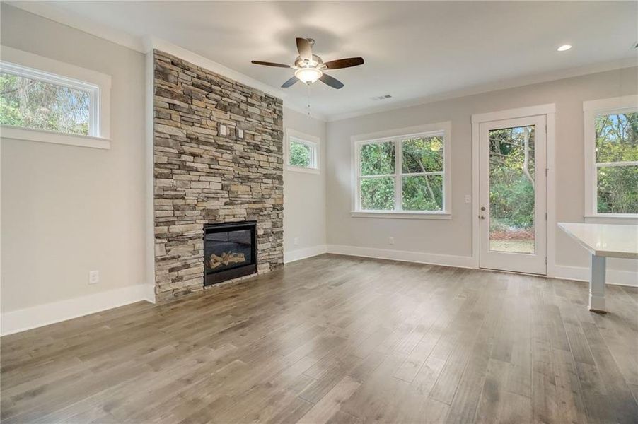 Unfurnished living room with a stone fireplace, ceiling fan, plenty of natural light, and light hardwood / wood-style flooring