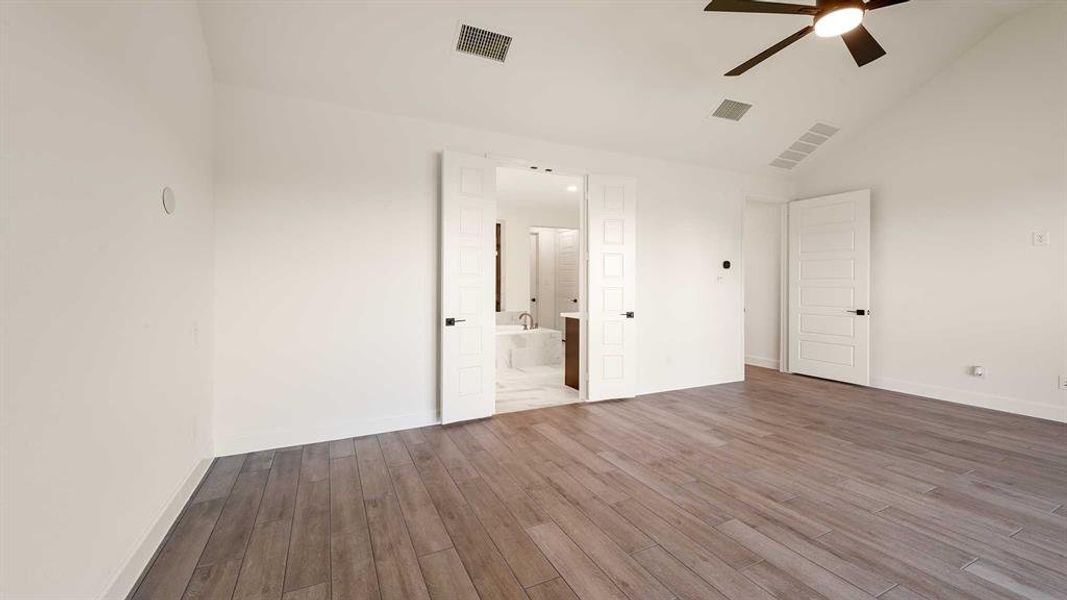 Unfurnished bedroom with connected bathroom, hardwood / wood-style flooring, high vaulted ceiling, and ceiling fan