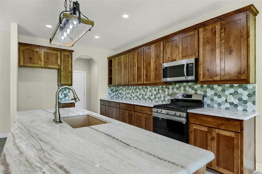 Kitchen with backsplash, light Quartzite counters, stainless steel appliances, decorative light fixtures, and sink