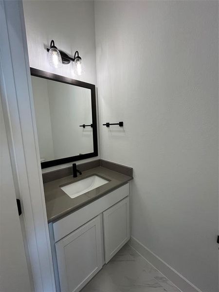 Guest half bath has quartz countertops, a framed mirror and Black hardware finishes