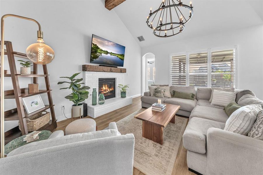 Living room featuring beamed ceiling, an inviting chandelier, high vaulted ceiling, hardwood / wood-style floors, and a fireplace