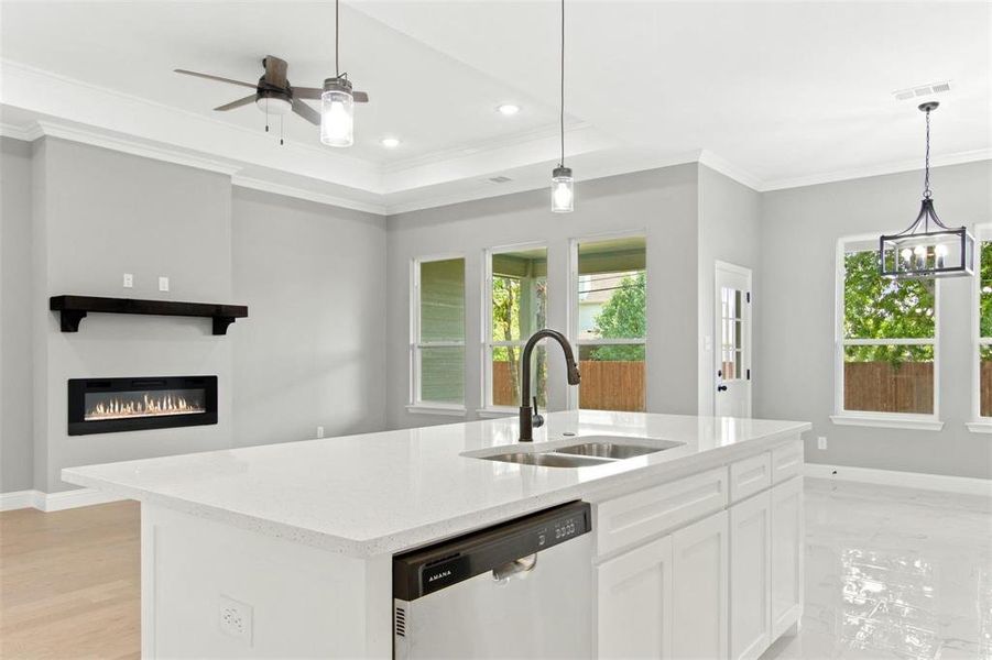 Kitchen featuring ceiling fan with notable chandelier, a kitchen island with sink, stainless steel dishwasher, light stone counters, and white cabinets