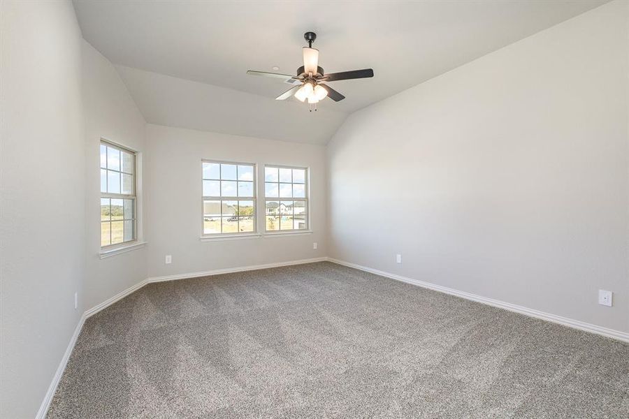 Carpeted spare room featuring ceiling fan and vaulted ceiling