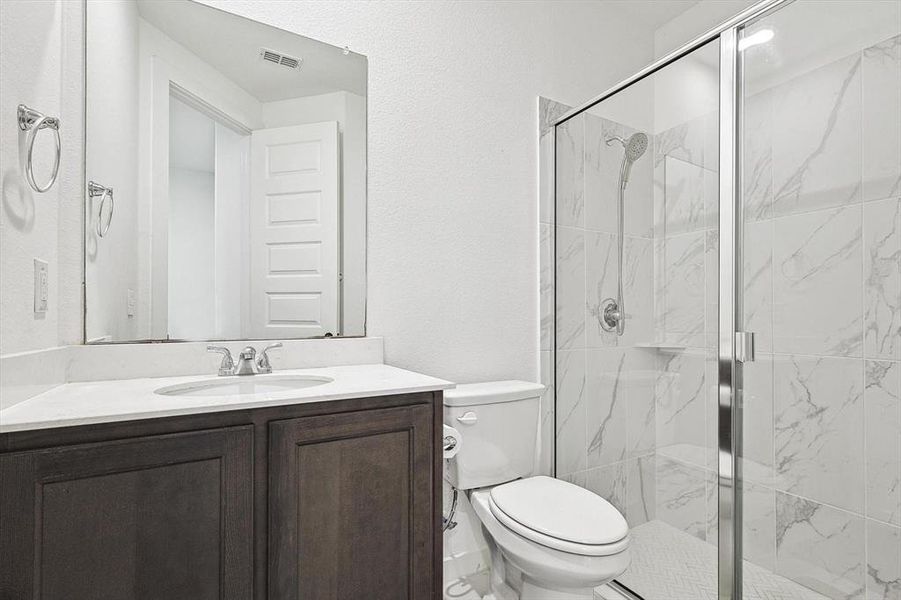 Bathroom with vanity, a shower with shower door, and toilet