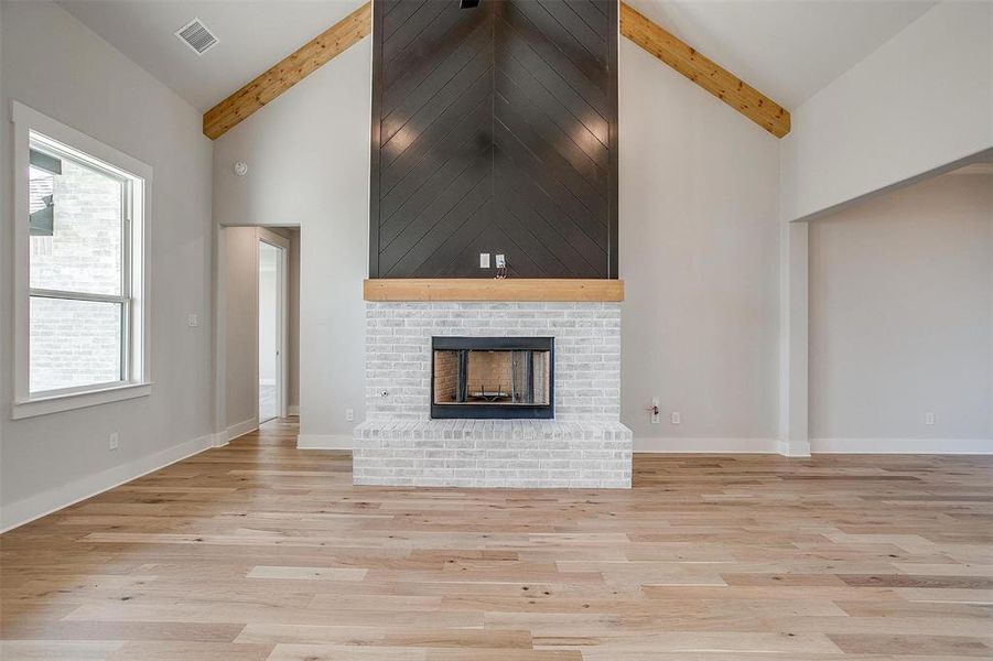 Unfurnished living room with high vaulted ceiling, beam ceiling, a brick fireplace, and light wood-type flooring