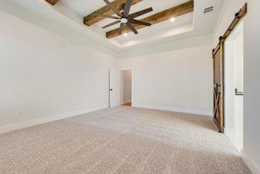 Empty room with a barn door, light colored carpet, a raised ceiling, and ceiling fan