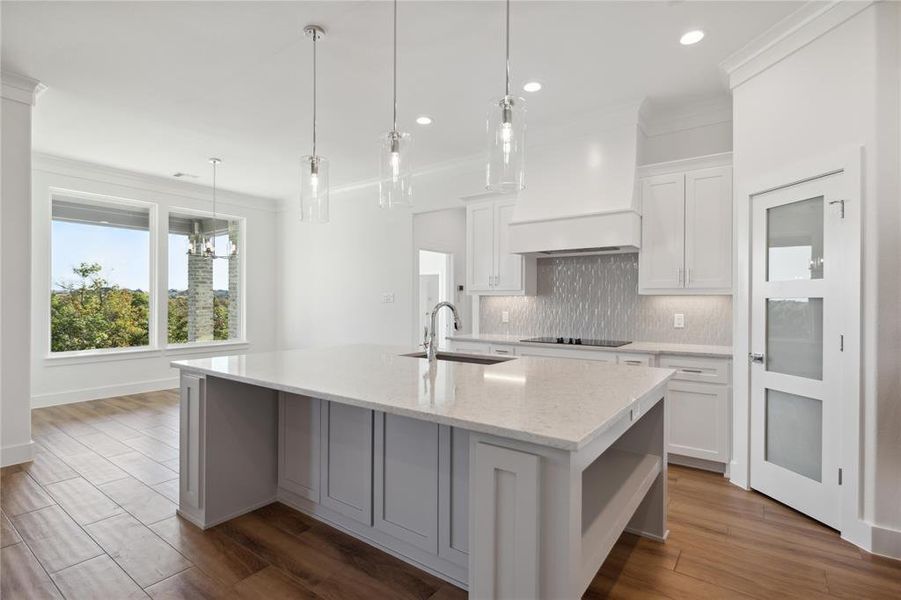 Kitchen featuring dark wood-type flooring, a kitchen island with sink, sink, and white cabinets