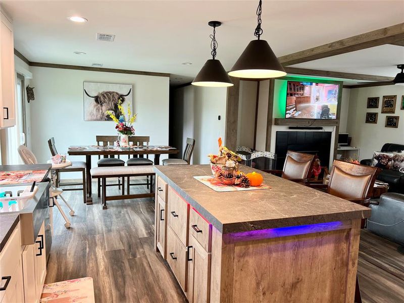 Kitchen with a center island, hanging light fixtures, a tiled fireplace, crown molding, and dark hardwood / wood-style floors