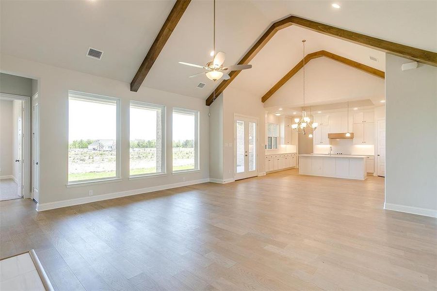 Unfurnished living room with light hardwood / wood-style flooring, sink, ceiling fan with notable chandelier, beam ceiling, and high vaulted ceiling