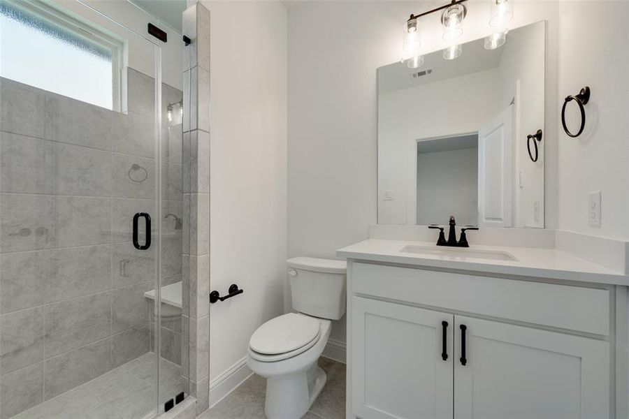 Bathroom featuring tile patterned flooring, a shower with shower door, toilet, and vanity