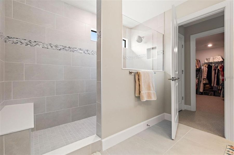 The shower in the primary bathroom has the upgraded, oversized walk-in shower with sitting bench and floor-to-ceiling tile.