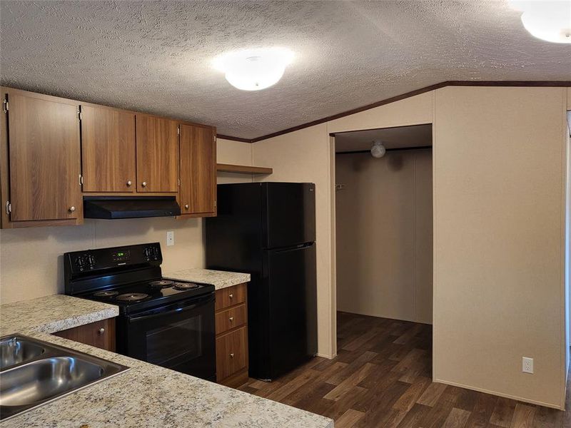 Kitchen featuring ornamental molding, black appliances, lofted ceiling, and dark wood-type flooring