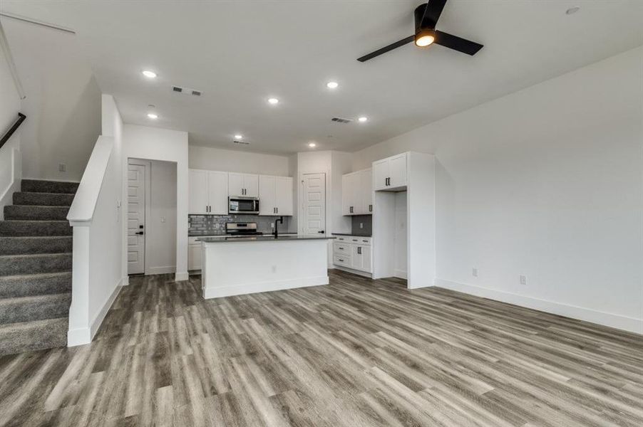 Kitchen featuring light hardwood / wood-style flooring, an island with sink, ceiling fan, white cabinetry, and appliances with stainless steel finishes