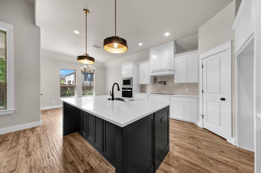 Kitchen featuring custom exhaust hood, light hardwood / wood-style floors, backsplash, and white cabinetry
