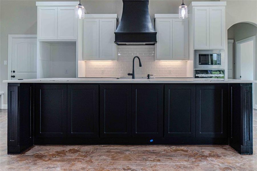 Kitchen with white cabinetry, decorative backsplash, hanging light fixtures, and custom range hood