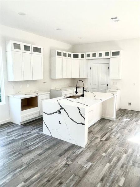 Kitchen with white cabinetry, light stone counters, an island with sink, wood-type flooring, and sink