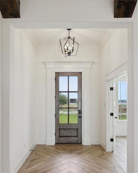 Doorway featuring a notable chandelier, ornamental molding, and light parquet flooring