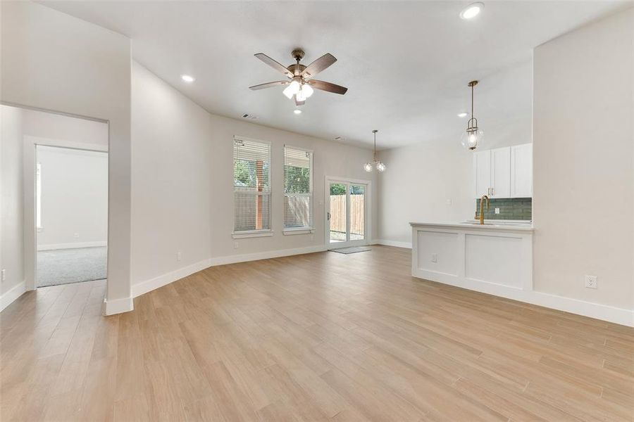 Unfurnished living room with ceiling fan with notable chandelier and light hardwood / wood-style flooring