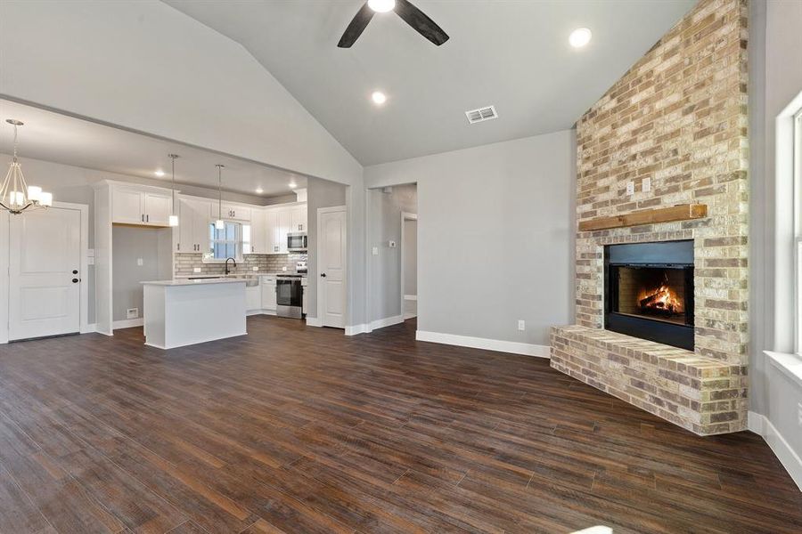 Unfurnished living room featuring high vaulted ceiling, dark hardwood / wood-style floors, a brick fireplace, and ceiling fan