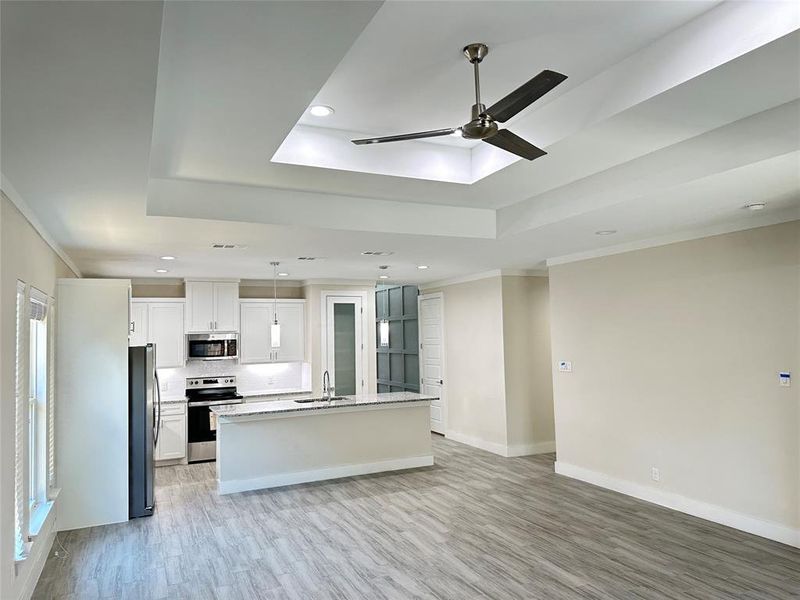 Kitchen featuring a center island with sink, ceiling fan, a tray ceiling, appliances with stainless steel finishes, and sink