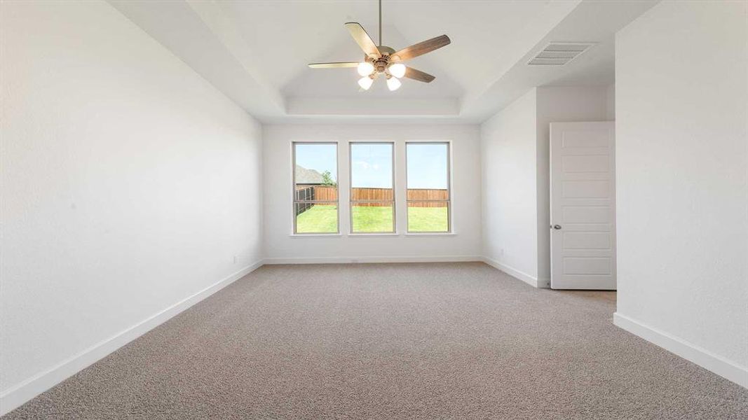 Unfurnished room featuring light colored carpet, a tray ceiling, and ceiling fan