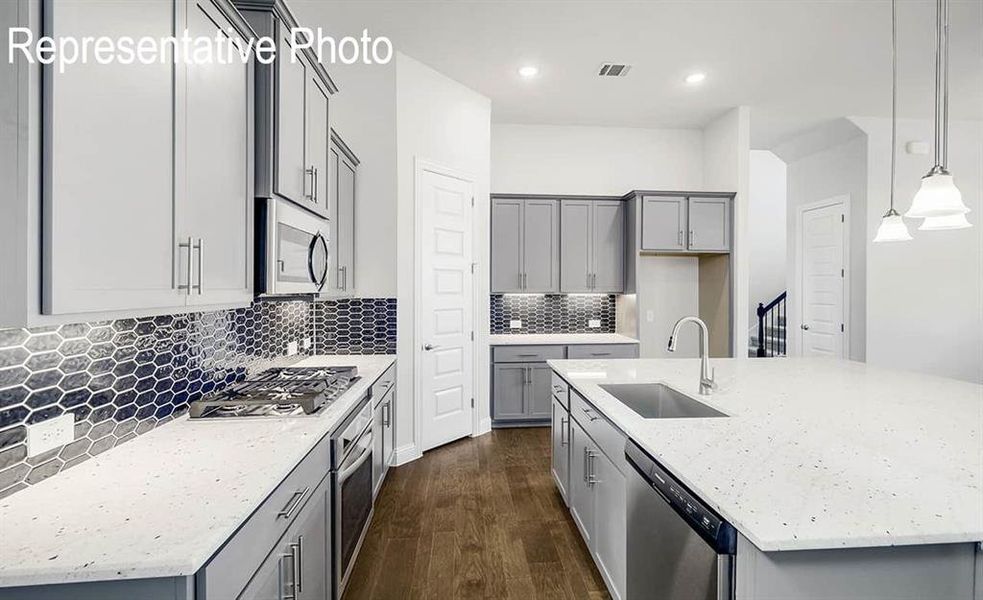 Kitchen with light stone counters, pendant lighting, sink, stainless steel appliances, and dark hardwood / wood-style flooring