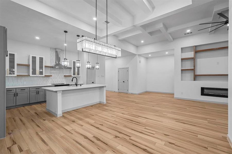 Kitchen with wall chimney exhaust hood, pendant lighting, light hardwood / wood-style flooring, a kitchen island with sink, and ceiling fan