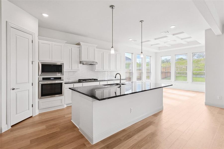 Kitchen with light hardwood / wood-style flooring, an island with sink, beam ceiling, coffered ceiling, and appliances with stainless steel finishes