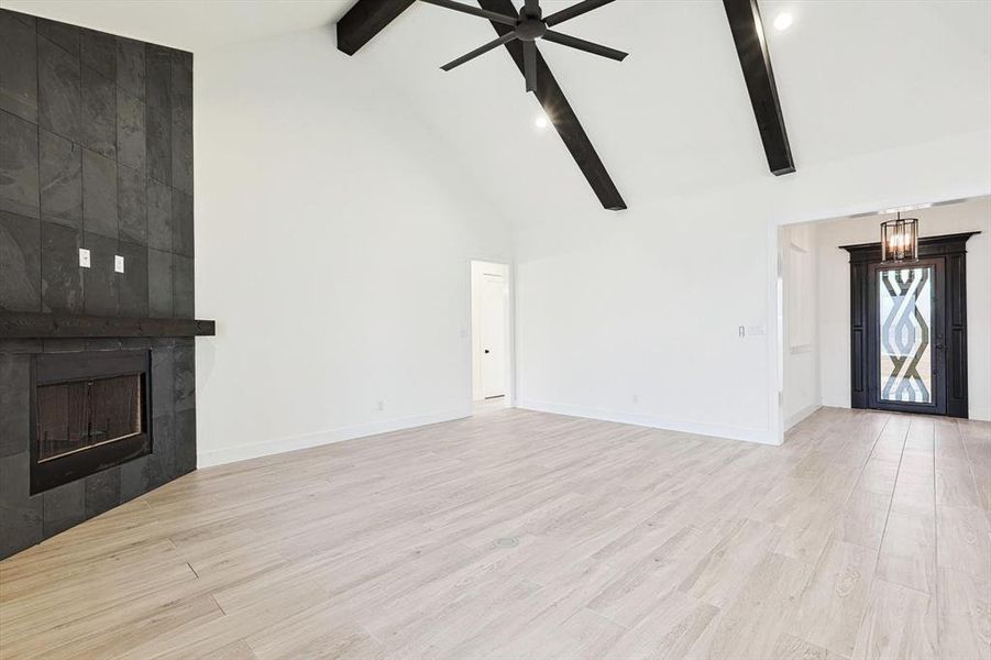 Unfurnished living room featuring light hardwood / wood-style floors, a tiled fireplace, ceiling fan, and high vaulted ceiling