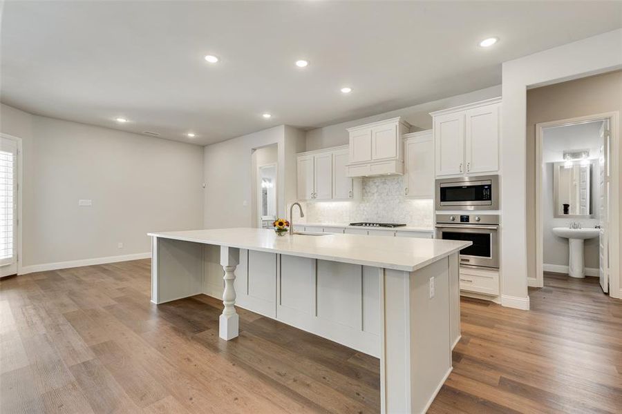 Kitchen with a large island, appliances with stainless steel finishes, light wood-type flooring, and white cabinetry