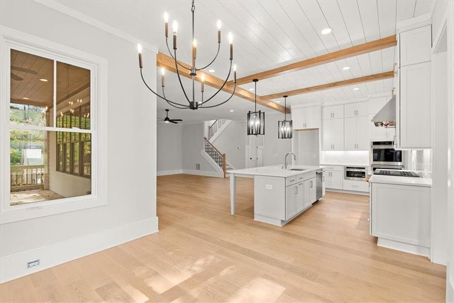 Kitchen featuring sink, light hardwood / wood-style flooring, an island with sink, white cabinetry, and beamed ceiling