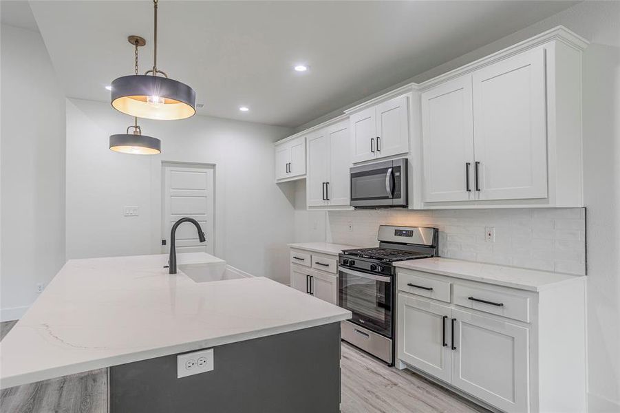 Kitchen featuring light wood-type flooring, backsplash, a kitchen island with sink, stainless steel appliances, and sink