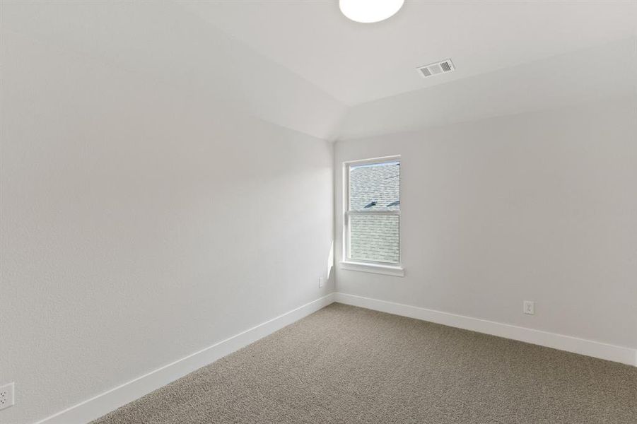 Carpeted spare room featuring vaulted ceiling