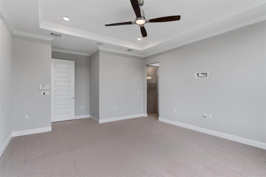 primary bedroom w/ high tray ceiling and ceiling fan