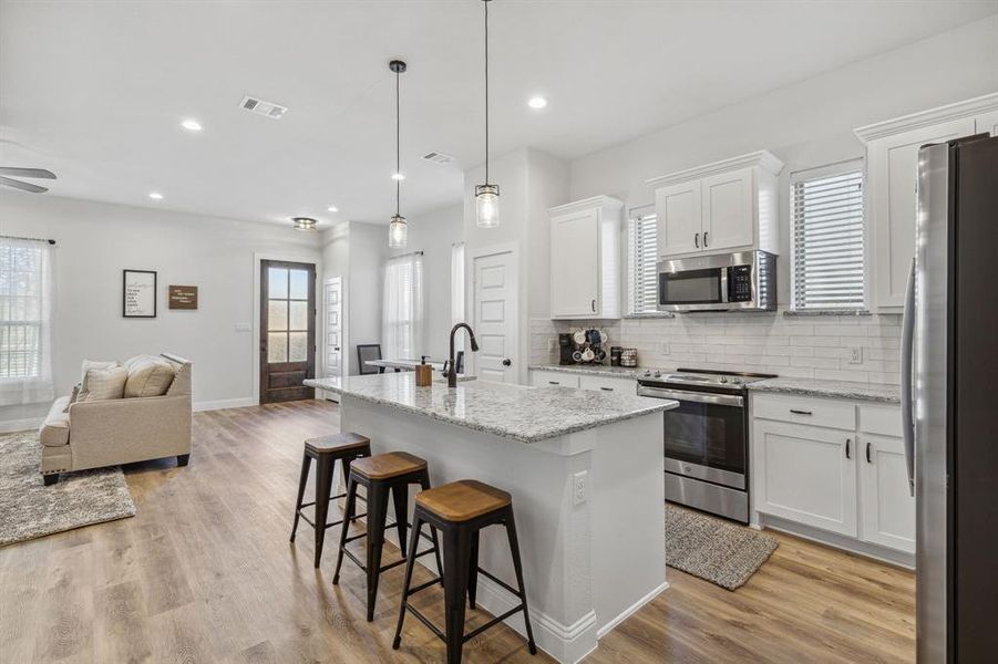 Kitchen featuring white cabinets, an island with sink, stainless steel appliances, light hardwood / wood-style floors, and decorative light fixtures