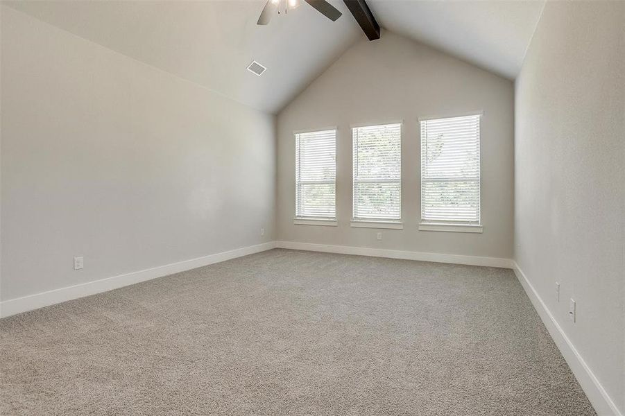 Carpeted empty room featuring lofted ceiling with beams and ceiling fan