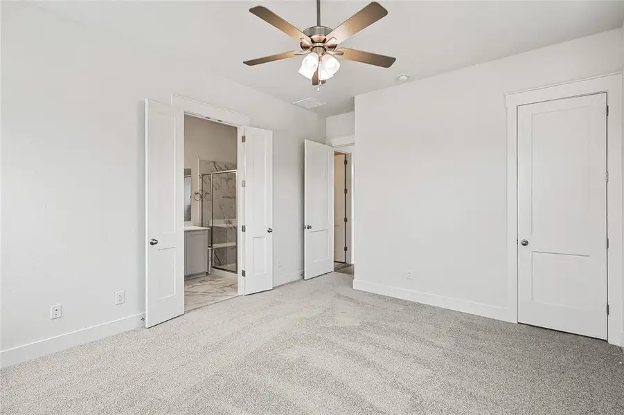 Unfurnished bedroom featuring light carpet, ensuite bath, and ceiling fan