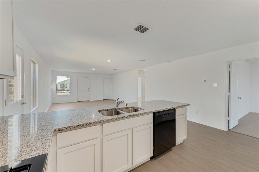 Kitchen with light stone countertops, dishwasher, sink, and white cabinets