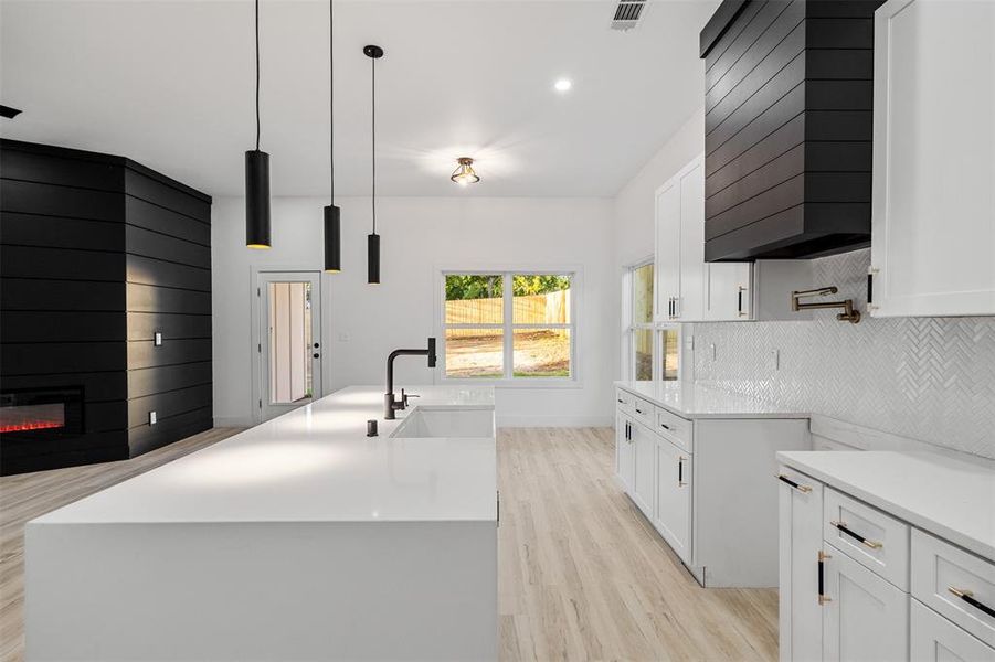 Kitchen with pendant lighting, an island with sink, and white cabinets