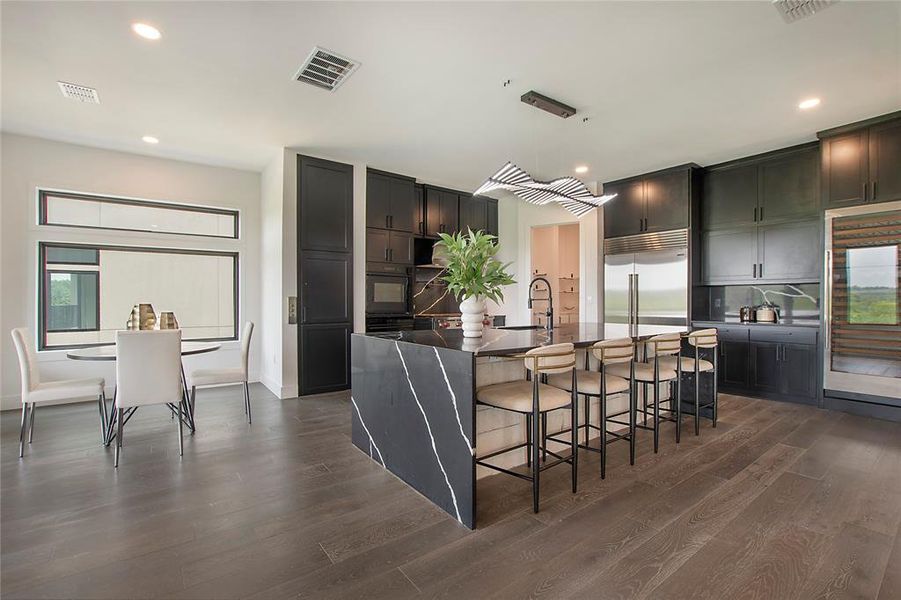 Kitchen featuring dark hardwood / wood-style floors, a center island with sink, oven, a breakfast bar, and built in refrigerator